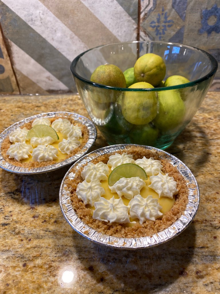 Mini Key Lime pies in a graham cracker crust and whip cream topping and a wedge of key lime,
